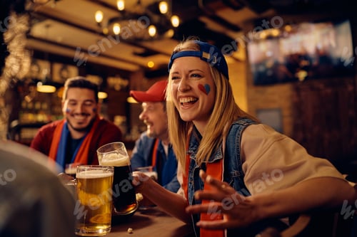 Preview: Happy sports fan and her friends having fun while drinking beer in a pub.