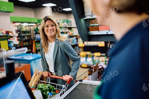 Preview: Happy woman talking to cashier at cash register in supermarket.
