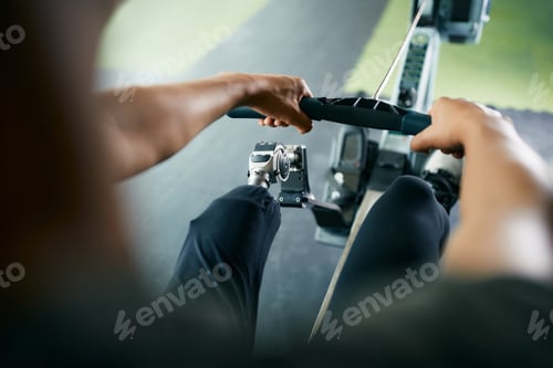 Preview: Close up of sportsman with disabled leg exercising on rowing machine in gym.