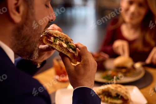Preview: Close up of businessman tasting club sandwich while eating in restaurant.