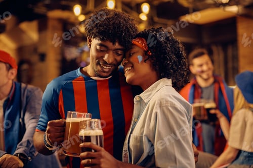 Preview: Black couple of sports fans toasting with beer after watching a match in a bar.