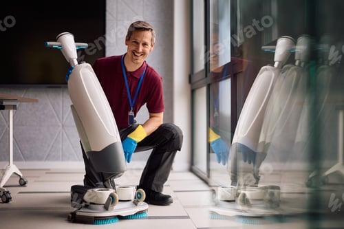 Preview: Happy janitor cleaning office floor with scrubber machine and looking at camera.