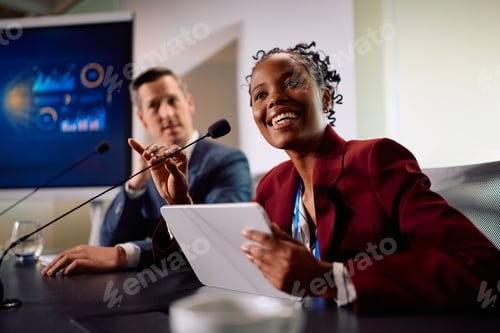 Preview: Happy black business panel speaker talking into microphone during a conference.