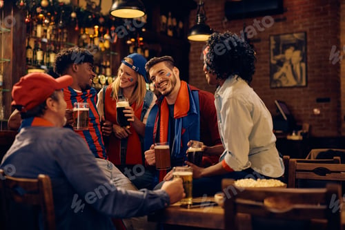 Preview: Happy sports fan talking to his friends while drinking beer in a bar.