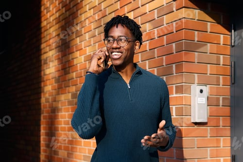 Preview: Young happy black man talking on smartphone on city street.