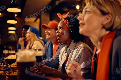 Preview: Multiracial group of sports fans watching match with anticipation in a bar.