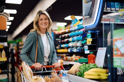 Preview: Happy woman at cash register in supermarket looking at camera.