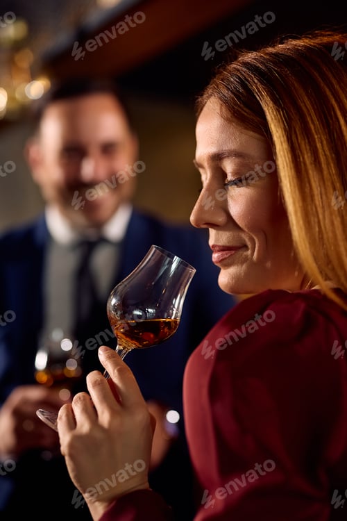 Preview: Smiling woman tasting cognac while drinking in a bar.