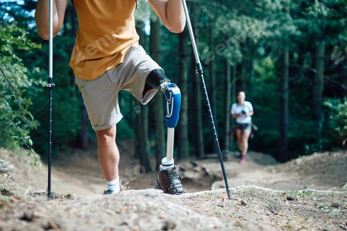 Preview: Unrecognizable man with bionic leg using hiking poles in the forest.