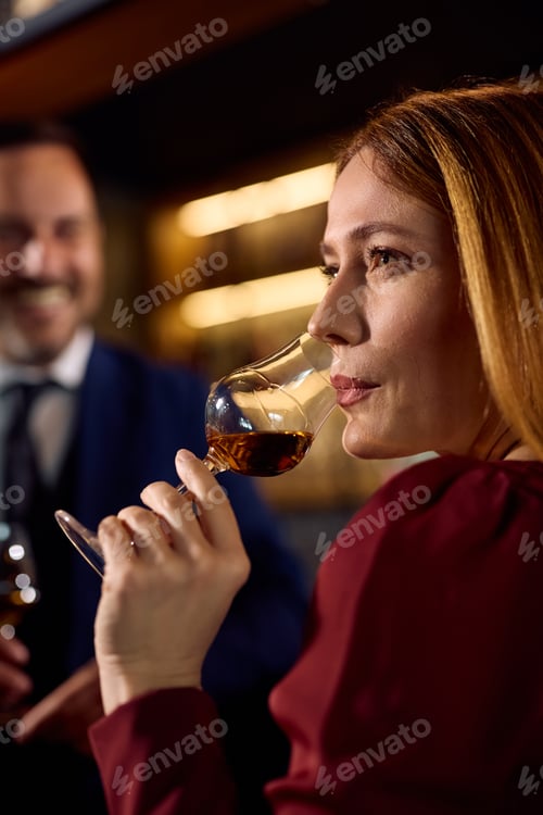 Preview: Mid adult woman enjoying in glass of brandy on in a bar.