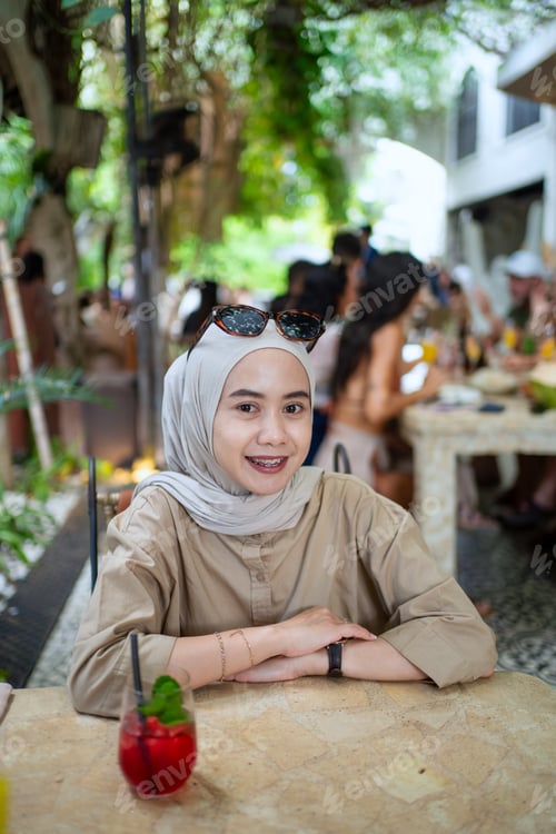 Preview: Indonesian Muslim woman relaxing at cafe table with fresh drink