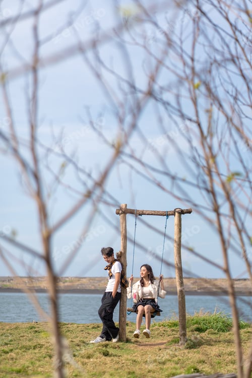 Preview: Young Asian Gen Z Couple Relaxing by Water with Wooden Swing