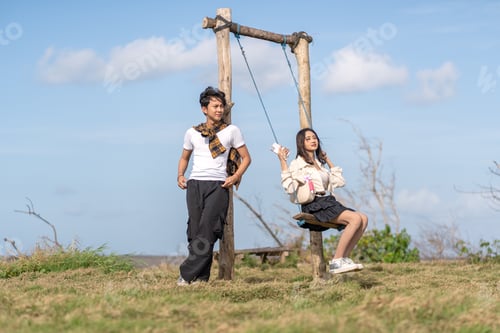 Preview: Young Asian Gen Z Couple with Rustic Swing Under Blue Sky