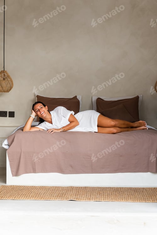 Preview: Young woman smiling while lying in bed, feeling comfortable and relaxed in her bedroom