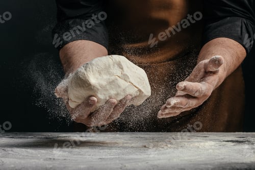 Preview: Baker holding fresh dough with flying flour particles in dark moody bakery scene artisan baking conc