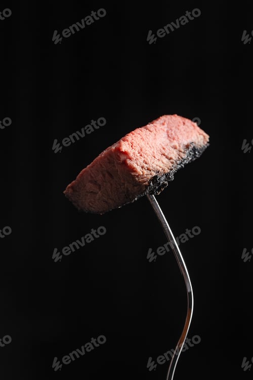Preview: Medium rare steak on fork against black background
