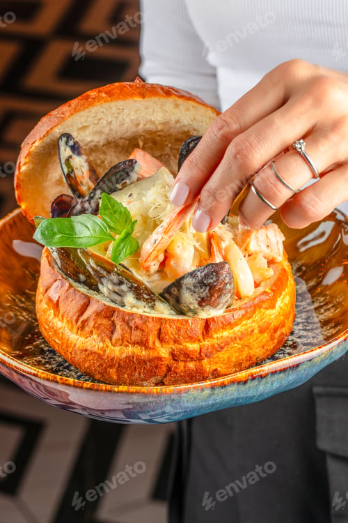 Preview: Hand taking shrimp from creamy seafood chowder served in artisan bread bowl