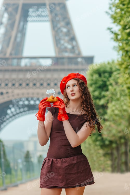 Preview: Young woman holding croissant with birthday candle near Eiffel Tower in Paris