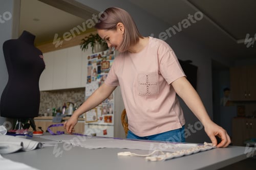 Preview: Woman measuring fabric on a worktable while sewing with a dress form in a home studio
