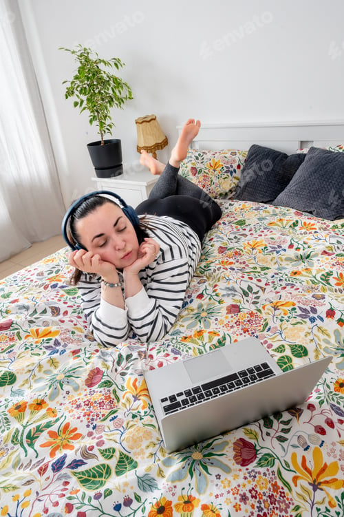 Preview: Woman taking online class from bed with laptop and headphones