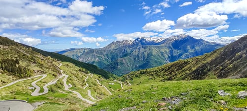 Preview: Scenic view of the Pyrenees mountains with winding roads, lush green hills, and a clear blue sky in