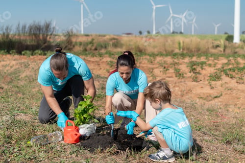 Preview: Volunteer Family Team Planting Trees and Seedlings Together in Open Field with Wind Turbines in Back
