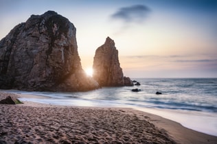 Sunset at Ursa Beach Sea stack, Portugal. Atlantic Ocean Foamy waves rolling to sandy beach. Holiday