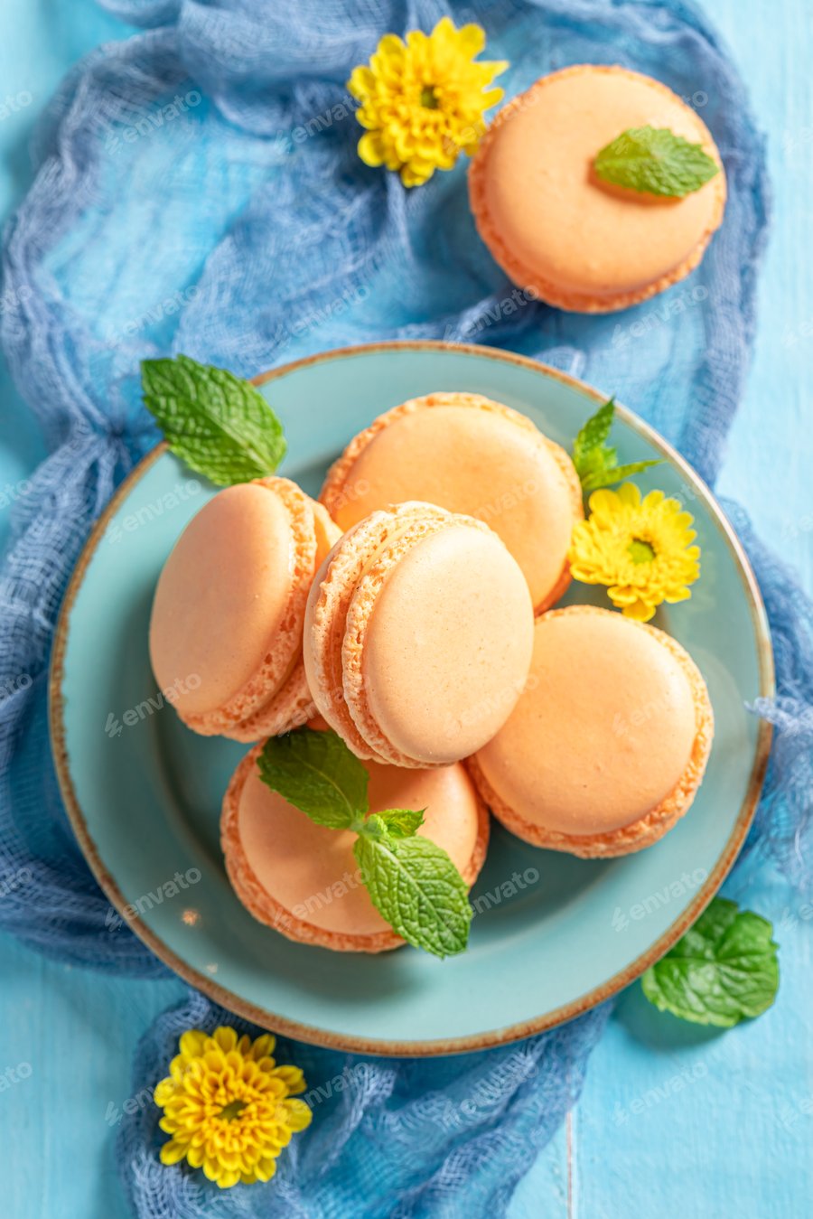 Cover for Delicious orange macaroons on blue table and yellow flowers