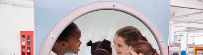 Schoolgirls looking in a magnifying mirror at science centre