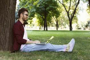 Man sitting on grass with laptop outdoors