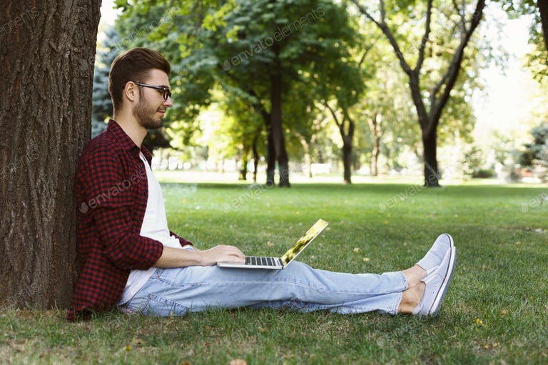 Man sitting on grass with laptop outdoors