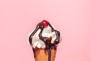 melting ice cream cone with chocolate syrup and cranberry isolated on pink background