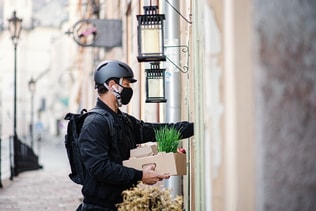 Delivery man courier with face mask delivering groceries in town