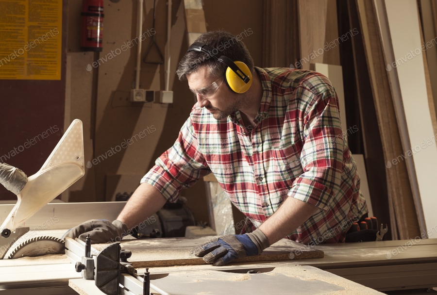 Worker in protective glasses and headphones cutting wood in a sa