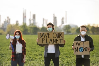 Group of young activists with placards standing outdoors by oil refinery, protesting