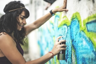 A young woman spray painting graffiti onto a wall.