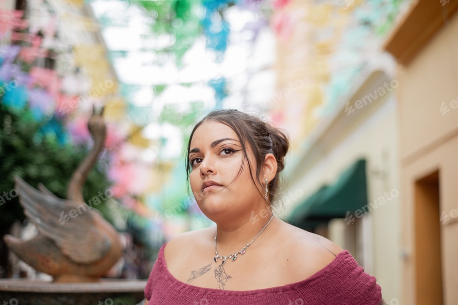 Cover for Street portrait of young woman looking at camera with multicolored flags in background. background,